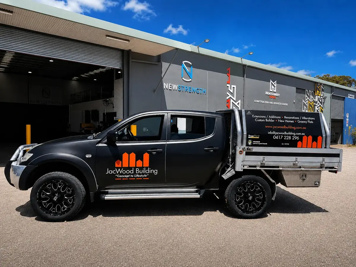 JacWood Building dual-cab Triton ute in matte black with orange logo graphics on the doors and tray canopy
