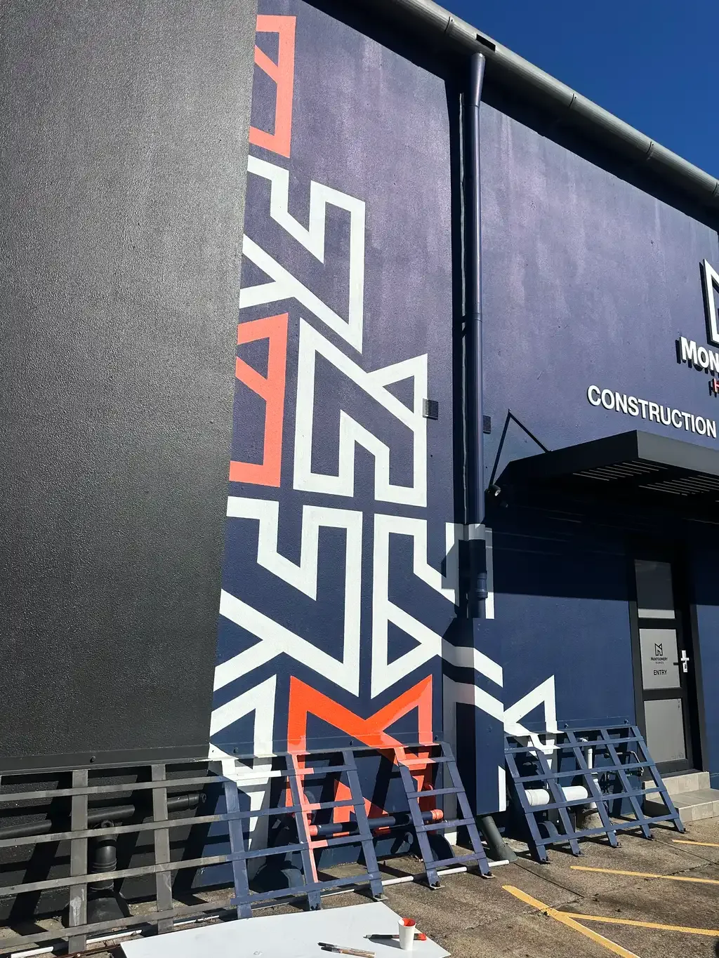 Montgomery Homes construction office wall in the same white, navy and orange livery, with the M pattern running down the corner of the building