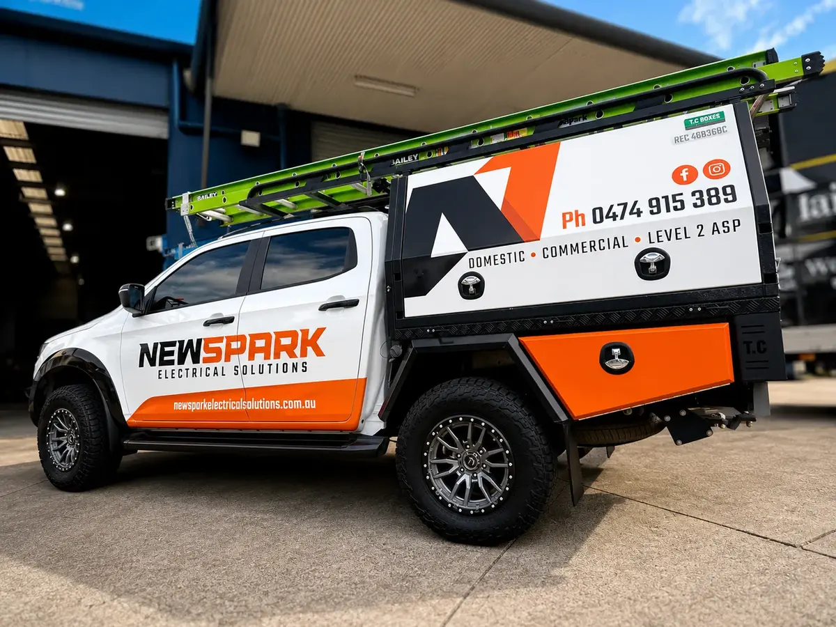 NewSpark Electrical Solutions dual-cab ute in white with orange and black canopy signage and a ladder on the roof rack