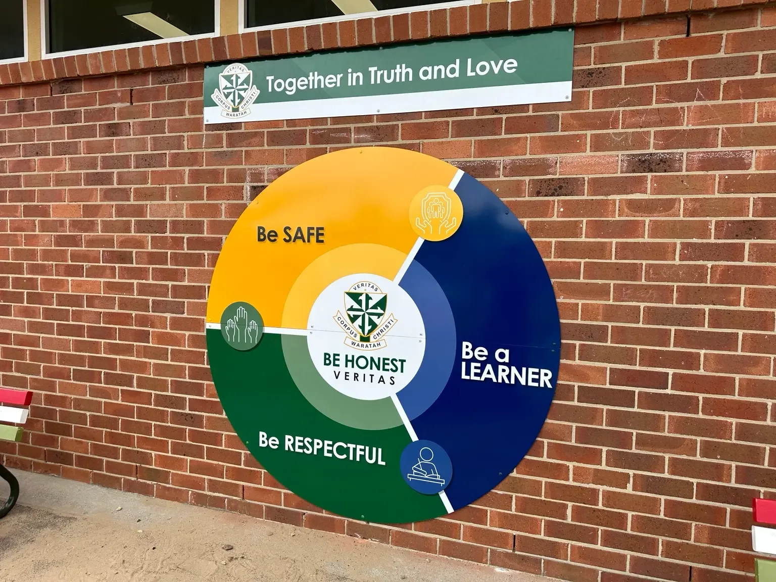 Corpus Christi Waratah school wall with a circular values sign and a Together in Truth and Love header panel
