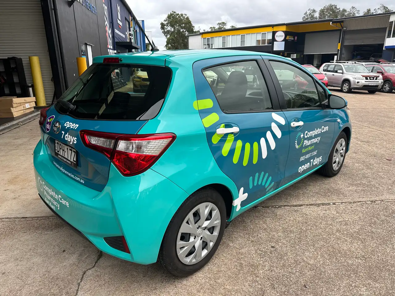 Rear three-quarter of the Complete Care Pharmacy Yaris, open 7 days beside the tail-light and the Complete Care Pharmacy Kurri Kurri logo with completecarepharmacies.com.au across the tailgate