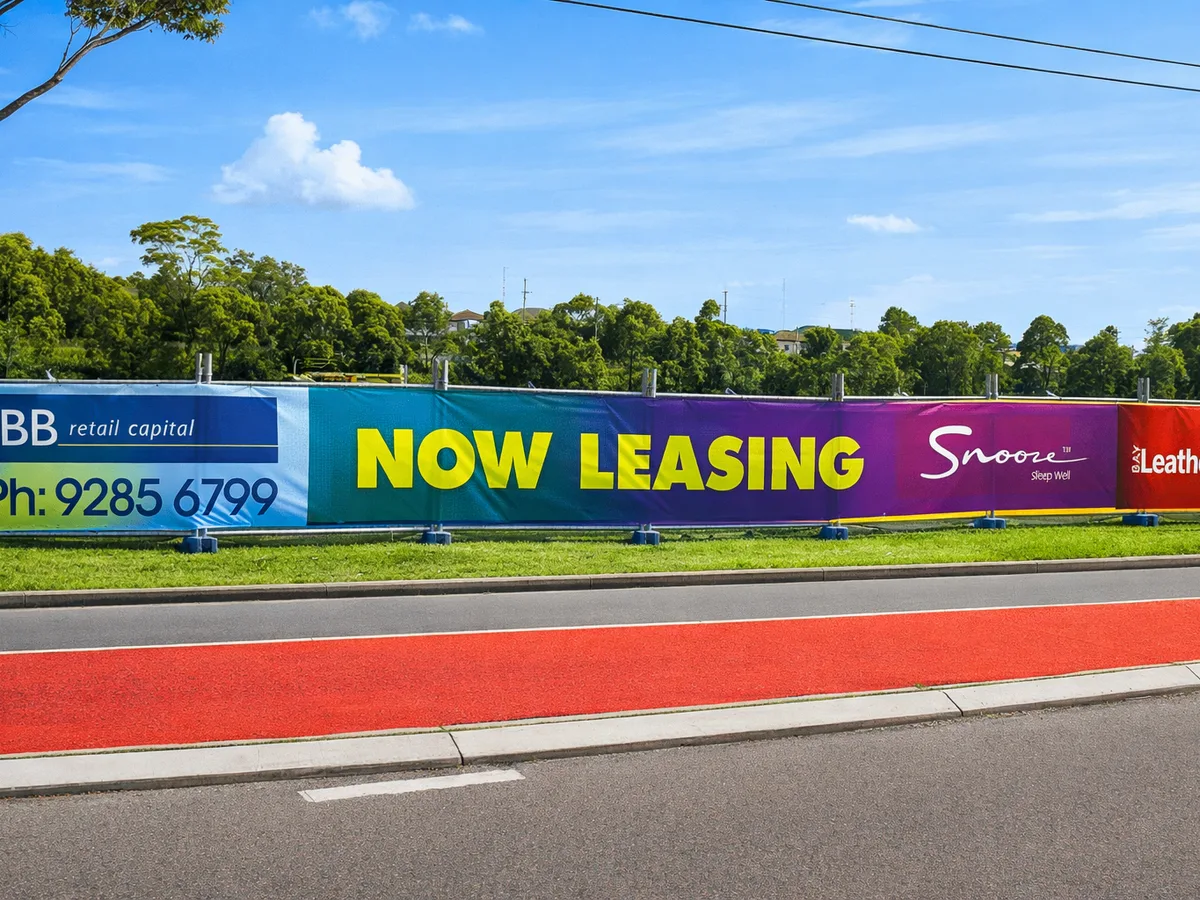 Printed mesh banner on temporary fencing, rainbow colours with yellow Now Leasing text and Snooze logo