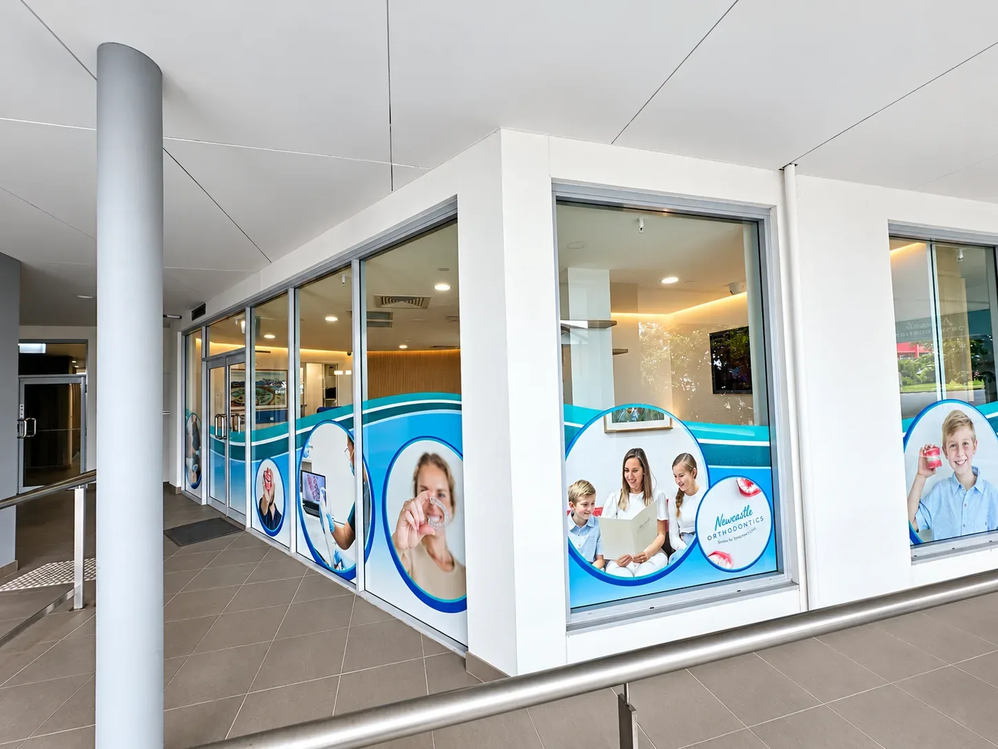 Full-colour one-way vision graphics with patient photos along the Newcastle Orthodontics glass frontage in Charlestown
