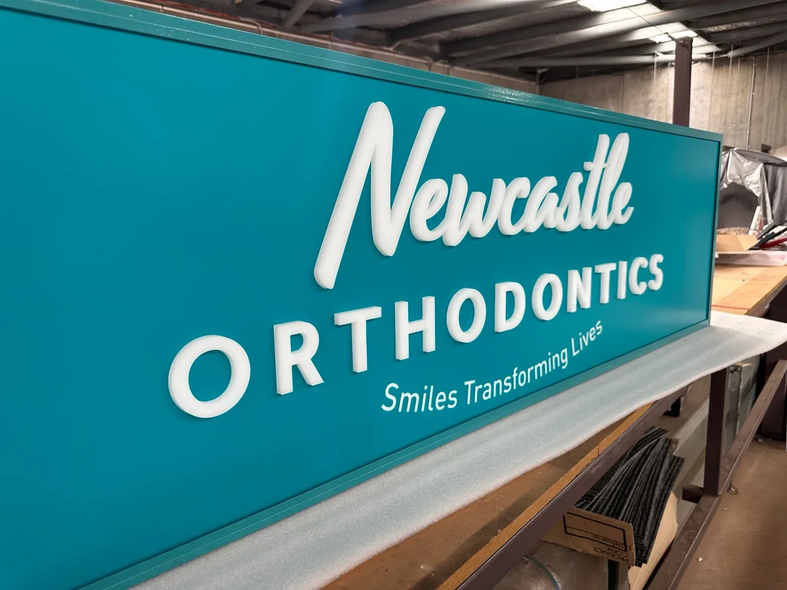 Teal Newcastle Orthodontics sign with raised white lettering, photographed in the Big Colour workshop