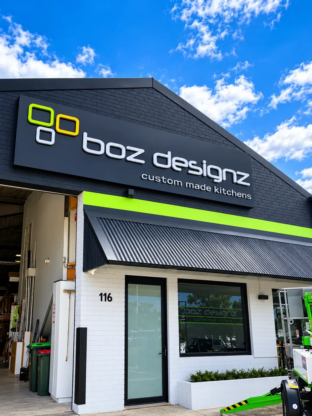 Boz Designz custom made kitchens showroom with its fascia sign over a charcoal facade, above a lime-green band and a dark awning