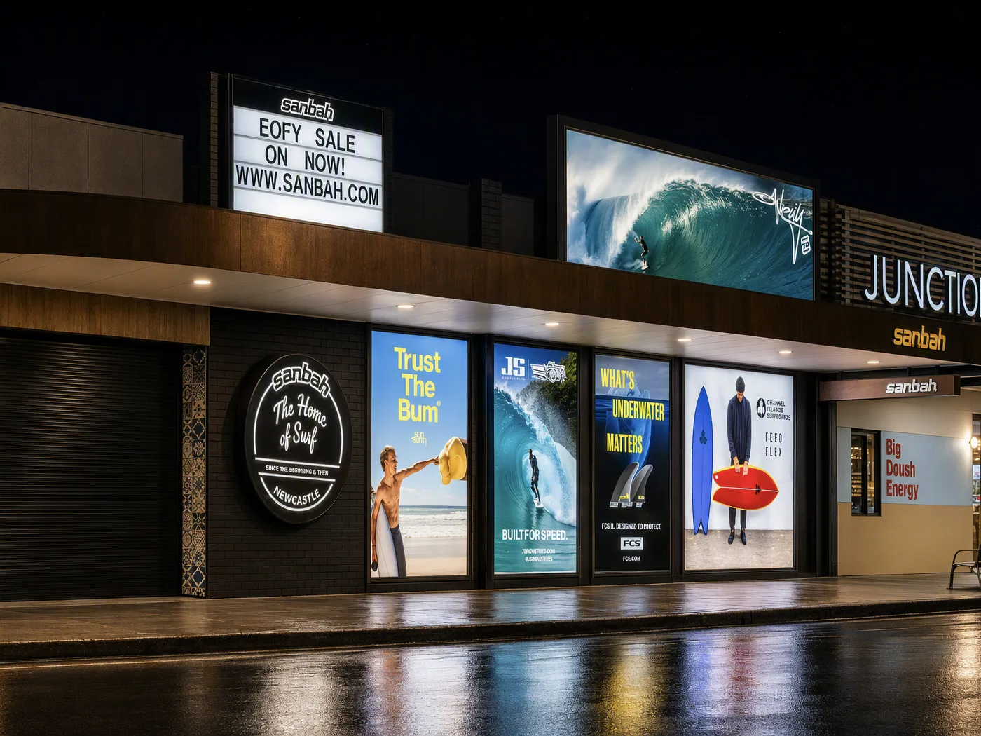 Sanbah surf shop at Junction Fair with illuminated lightbox signs and glowing window displays at night