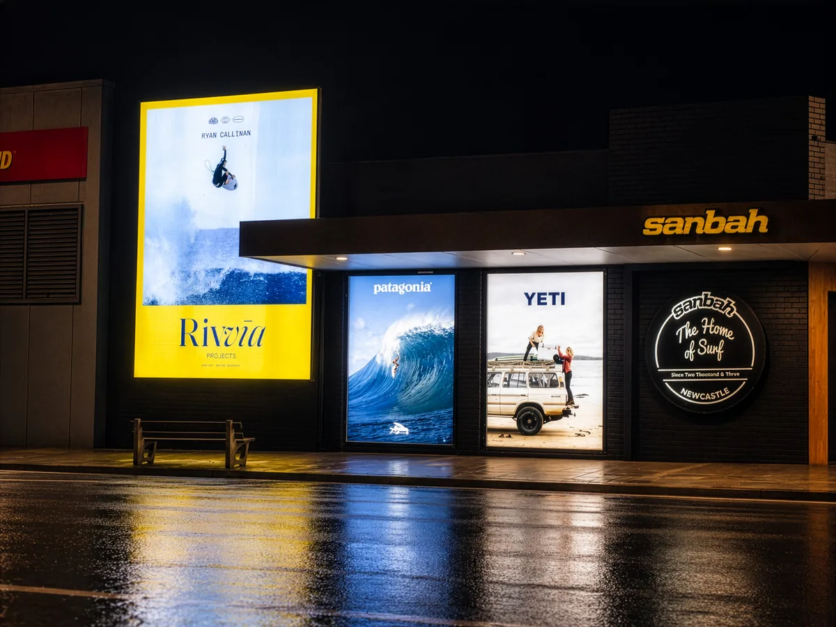 Sanbah surf shop illuminated lightbox posters and glowing round logo sign lighting up the street at night