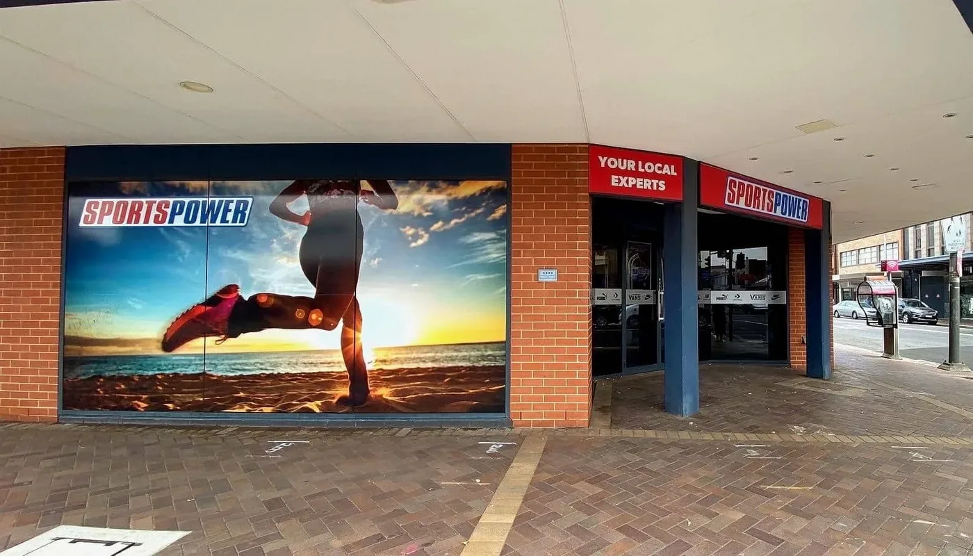Sports Power shopfront with a printed beach runner graphic across the window and a logo band on the glass doors