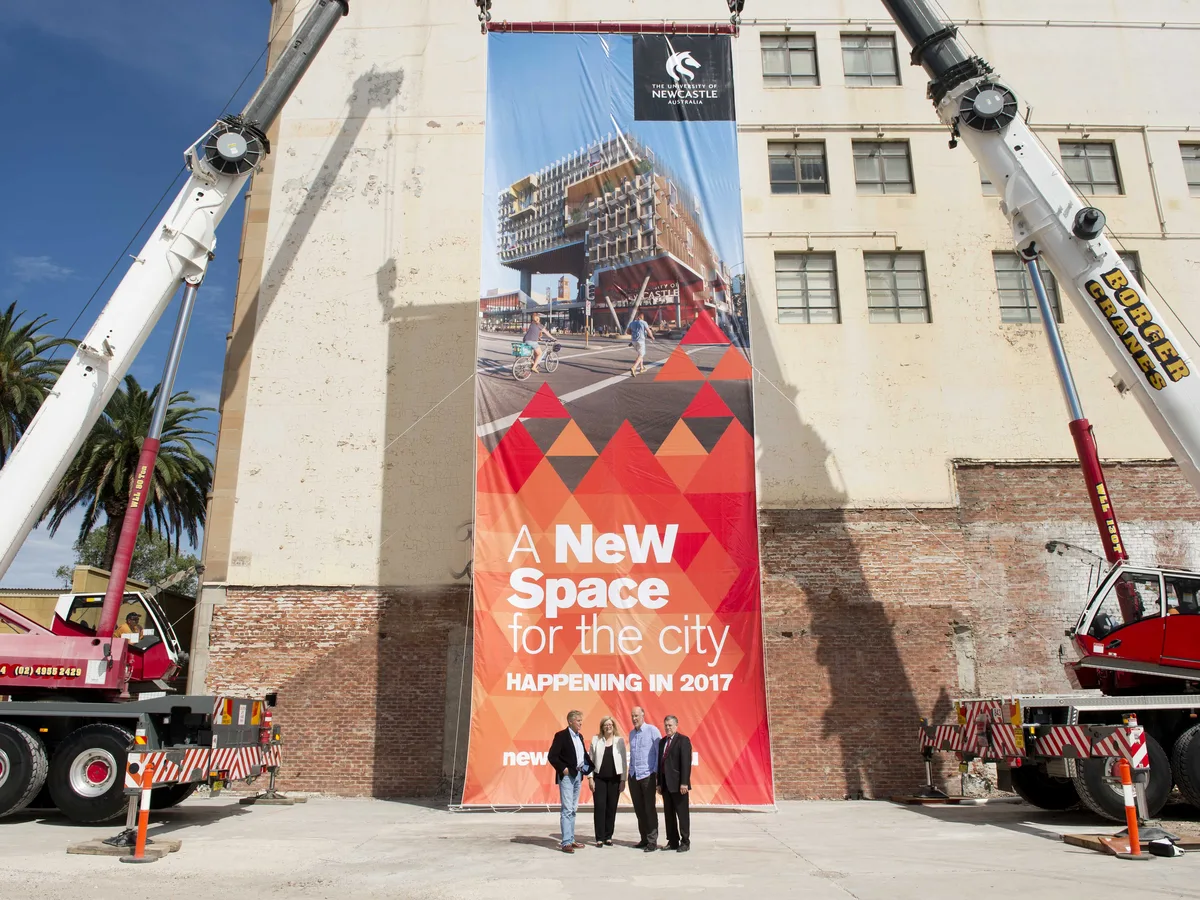 Tall University of Newcastle building banner in red and orange, lifted by two cranes