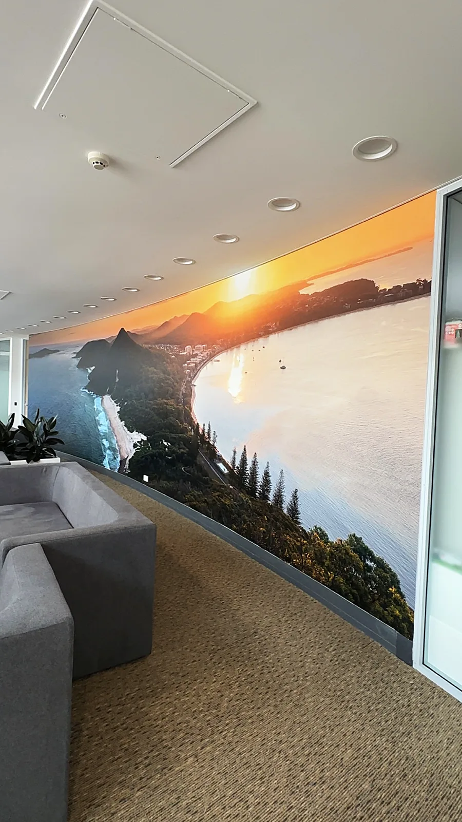 Full-height detail of the coastal sunset mural beside office greenery